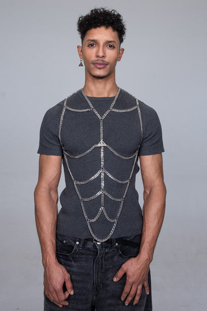 The logo of the fashionbrand Lorand Lajos is shown twice in this picture. Once on the body chain accessory and once on the logo earring. The chains draw a six pack  on to the gray fashionable street wear outfit