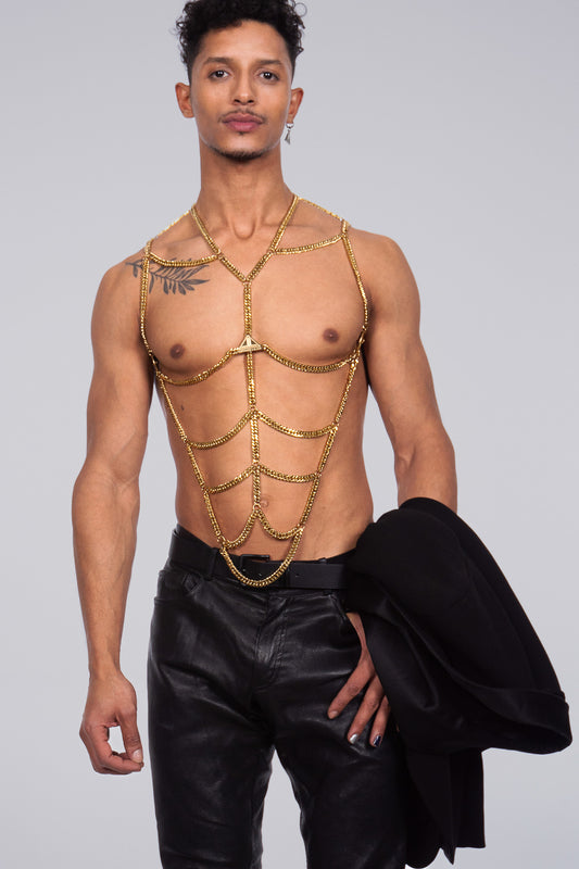 Product picture of a muscular, attractive, young man with masculin body chain  in sparkly gold, made by the fashion brand Lorand Lajos. He is topless and in leather pants.  